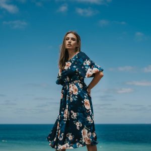 Stylish woman in a floral sundress posing by the sea in Istanbul, capturing a serene and vibrant summer moment.